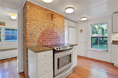 Kitchen with electric stove, light hardwood / wood-style floors, white cabinets, brick wall, and white refrigerator | Image 3