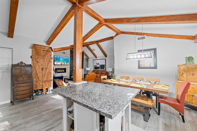 Dining room featuring baseboards, light wood-type flooring, a fireplace, visible vents, and vaulted ceiling with beams | Image 6