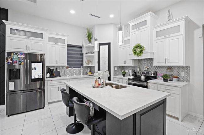 Kitchen featuring stainless steel appliances, a sink, light marble finish flooring, light countertops, and a center island with sink | Image 19
