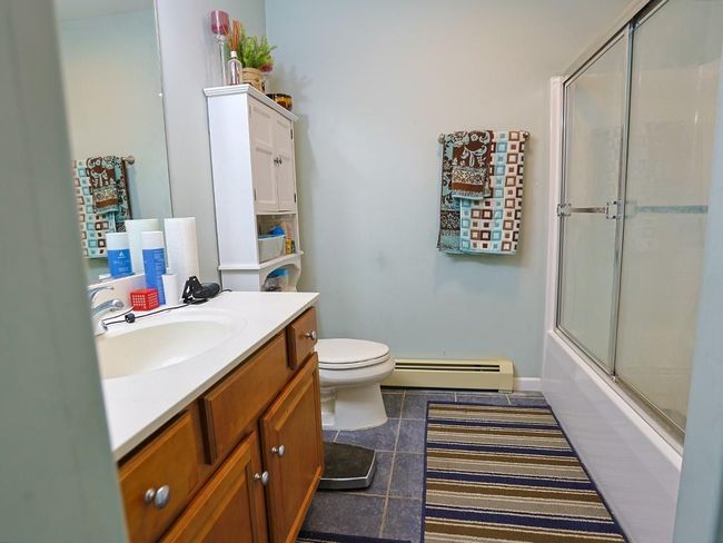 Full bath featuring tile patterned floors, toilet, vanity, baseboard heating, and shower / bath combination with glass door | Image 30