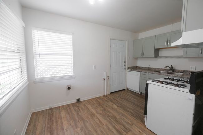 Kitchen with white dishwasher, range with gas cooktop, a sink, and wood finished floors | Image 6