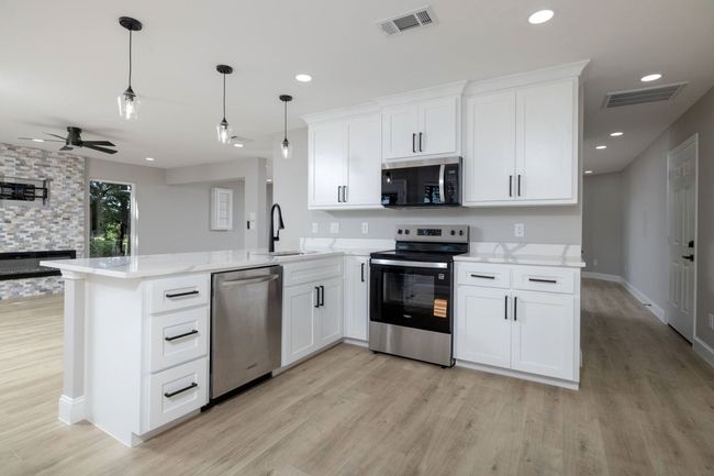Kitchen with appliances with stainless steel finishes, light wood finished floors, a peninsula, white cabinets, and a ceiling fan | Image 17