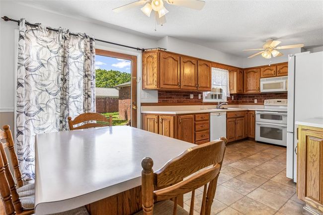 Kitchen featuring white appliances, a ceiling fan, tasteful backsplash, a sink, and brown cabinets | Image 39