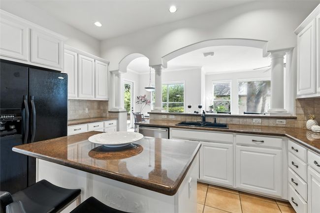 Kitchen featuring decorative columns, black fridge with ice dispenser, white cabinets, arched walkways, and recessed lighting | Image 16