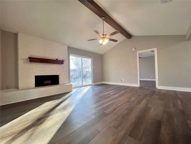 Unfurnished living room with ceiling fan, dark hardwood / wood-style flooring, lofted ceiling with beams, and a fireplace | Image 12