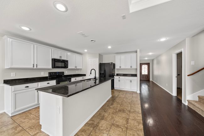 Kitchen with black appliances, white cabinetry, an island with sink, and recessed lighting | Image 16