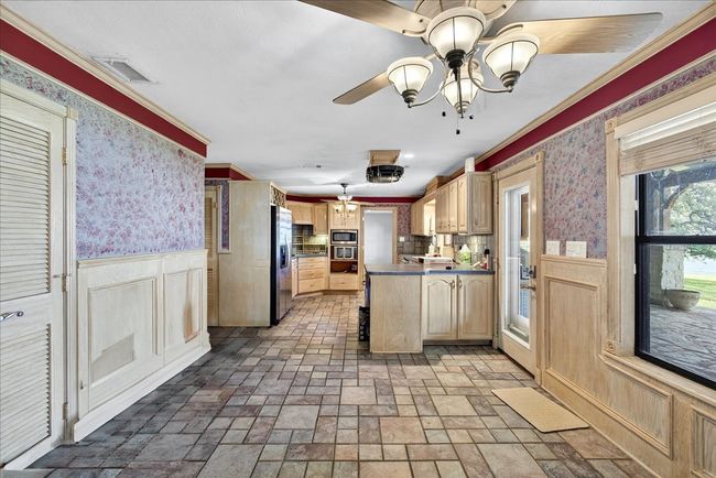Kitchen featuring appliances with stainless steel finishes, a peninsula, wallpapered walls, light brown cabinetry, and wainscoting | Image 19