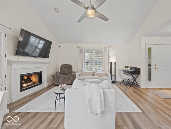 living room with a warm lit gas log fireplace, large ceiling fan & light, wood finished floors, with vaulted ceiling & windows to front porch area | Image 6