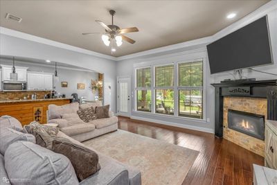 Living room featuring ornamental molding, ceiling fan, a fireplace, and wood flooring | Image 3