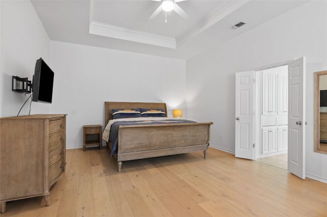 Bedroom featuring a raised ceiling, visible vents, ornamental molding, light wood-style floors, and baseboards | Image 23