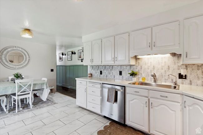 Kitchen with stainless steel dishwasher, white cabinetry, light countertops, light marble finish floors, and backsplash | Image 11