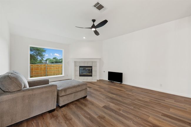 Living area with a ceiling fan, wood finished floors, and a tile fireplace | Image 17