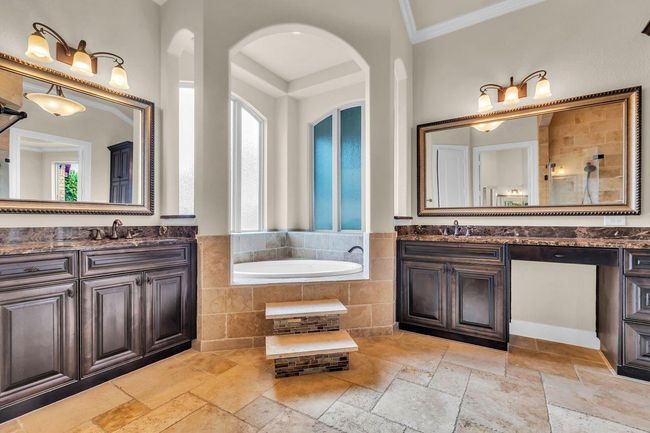 The luxurious primary bathroom boasts separate dual sinks with elegant countertops, offering plenty of space for two. A spacious jetted tub with built-in steps provides a relaxing spa-like retreat. | Image 21