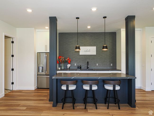 Kitchen featuring dark countertops, stainless steel refrigerator with ice dispenser, a breakfast bar area, and recessed lighting | Image 70