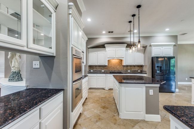 Kitchen with black appliances, crown molding, tasteful backsplash, glass insert cabinets, and white cabinetry | Image 12