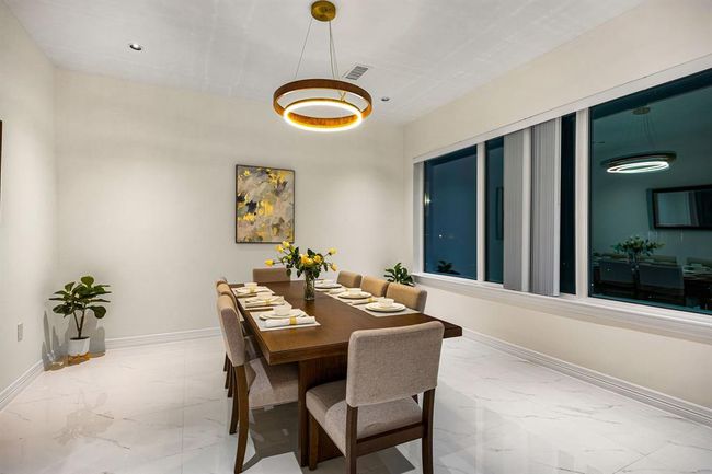 Indulge in elegant dining experiences in this exquisite dining room, where sophistication meets modern design. A stunning contemporary chandelier casts a warm, ambient glow across the marble flooring, while soaring ceilings and a grand picture window with tailored blinds enhance the room’s airy elegance. The perfect setting for hosting unforgettable gatherings with family and friends. | Image 18