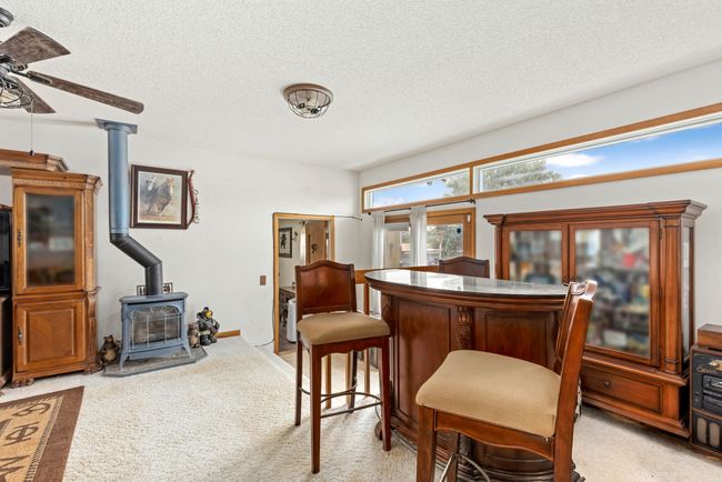 Dining space featuring a textured ceiling, a wood stove, a ceiling fan, and light colored carpet | Image 40
