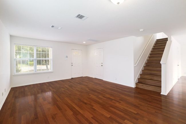 Unfurnished living room with wood finished floors, visible vents, baseboards, and stairs | Image 4