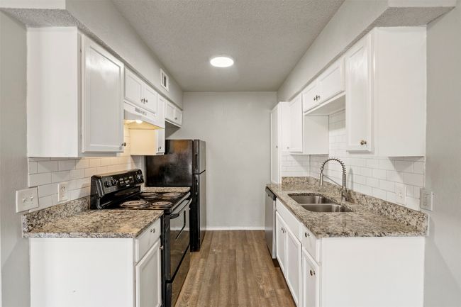 Kitchen featuring black range with electric stovetop, a sink, stainless steel dishwasher, under cabinet range hood, and baseboards | Image 9