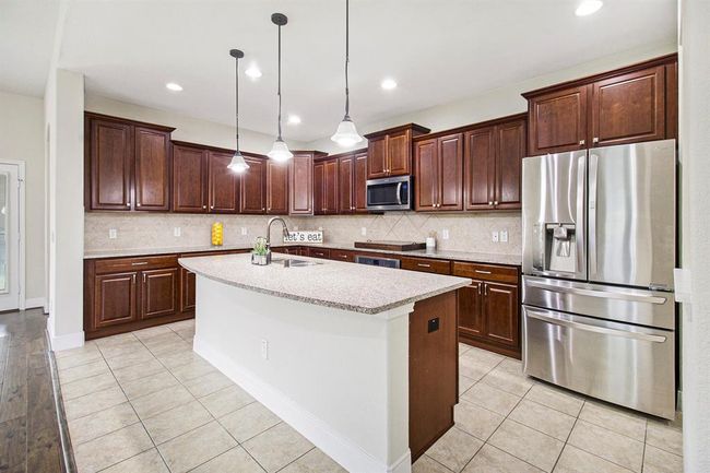 This kitchen features upgraded 42" Cherry wood cabinetry, a spacious island with granite countertops, stainless steel appliances, and modern pendant lighting. The tiled floor and ample storage make it both stylish and functional. | Image 8