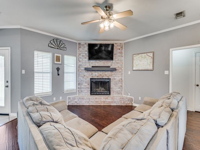 Living room featuring dark wood-style flooring, a fireplace, a ceiling fan, ornamental molding, and baseboards | Image 8