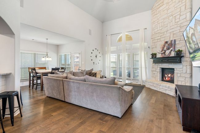 Living room with a stone fireplace, dark wood-type flooring, a towering ceiling, and a chandelier | Image 11
