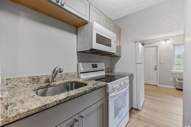 Kitchen featuring white appliances, a sink, a textured ceiling, gray cabinetry, and light wood-style floors | Image 6