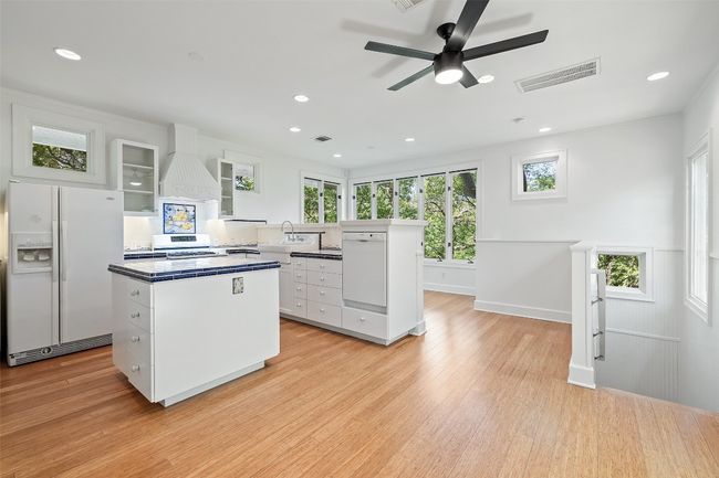 Kitchen featuring white fridge with ice dispenser, white cabinets, visible vents, a center island, and premium range hood | Image 7