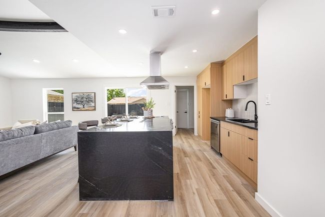 Kitchen featuring stainless steel dishwasher, light wood-style flooring, light brown cabinetry, a sink, and island range hood | Image 18