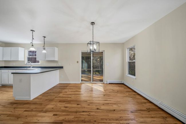 Kitchen with white cabinetry, a healthy amount of sunlight, dark countertops, light wood-style flooring, and a peninsula | Image 8