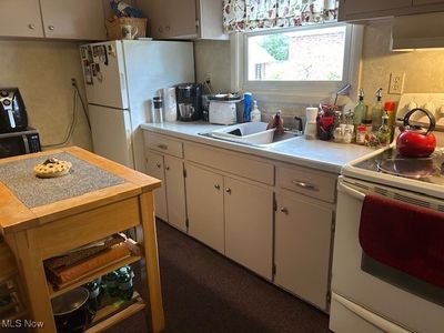 Kitchen featuring white cabinets, white appliances, exhaust hood, and sink | Image 2