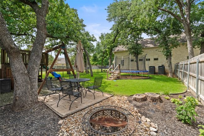 View of yard featuring an outdoor fire pit, a trampoline, central air condition unit, and a patio | Image 35