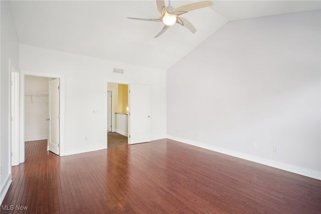 Unfurnished bedroom featuring a walk in closet, visible vents, wood finished floors, baseboards, and lofted ceiling | Image 15