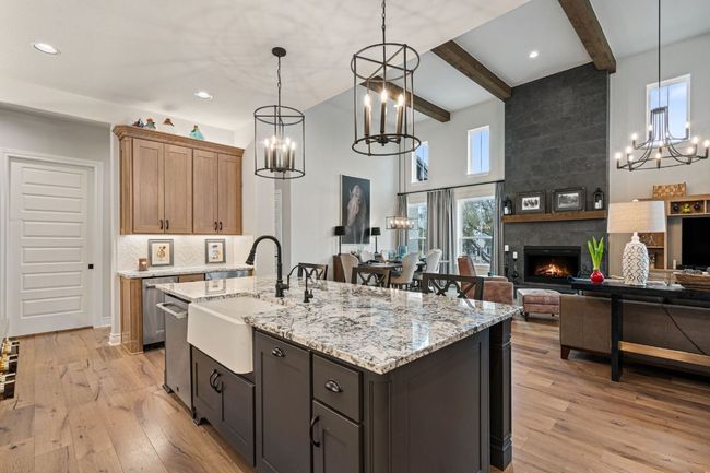 Kitchen view and living room view of a large fireplace, light stone counters, and light wood-style floors | Image 13