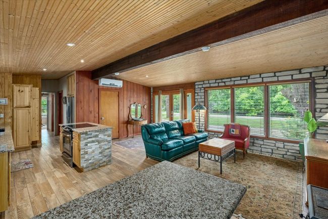 Living area with light wood-style flooring, wood walls, a wooden ceiling with exposed beams, and a wall mounted AC | Image 13