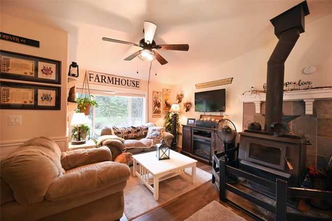 Living area with a wood stove, ceiling fan, wood finished floors, and lofted ceiling | Image 20