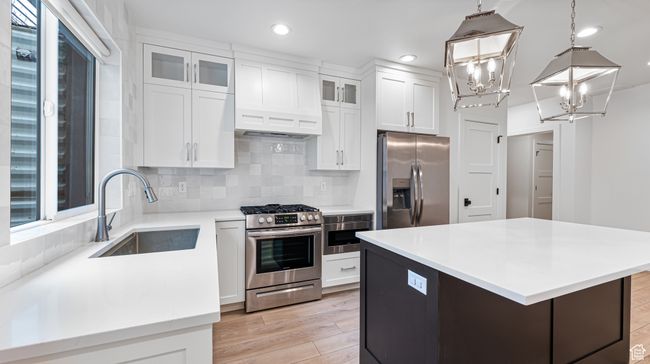 Kitchen with stainless steel appliances, a sink, backsplash, white cabinetry, and light countertops | Image 62