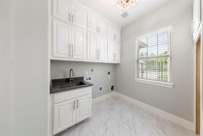 This spacious utility room is both practical and polished, offering ample cabinetry, sink, and a designated nook perfectly sized for an additional refrigerator or freezer. | Image 19