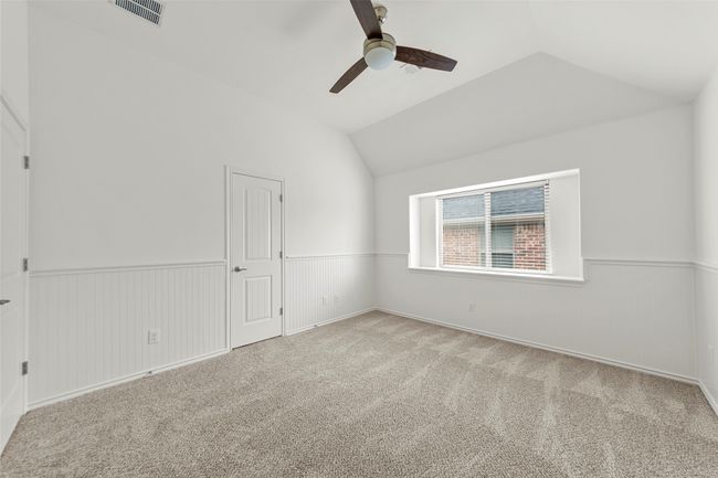 Empty room featuring visible vents, lofted ceiling, carpet flooring, a wainscoted wall, and a ceiling fan | Image 27