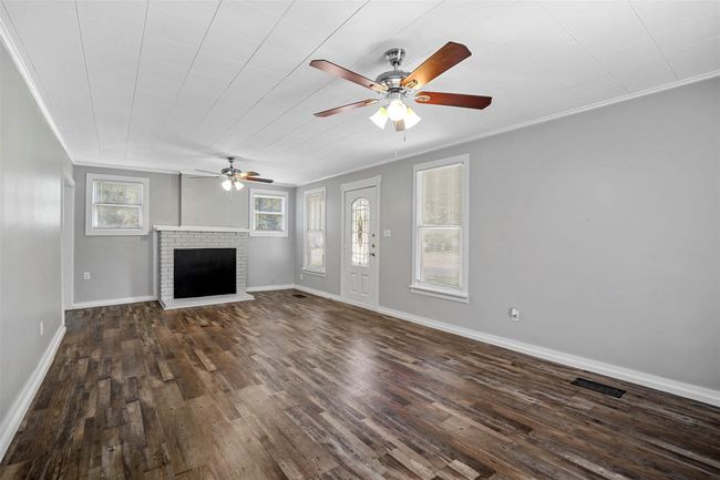Unfurnished living room with ceiling fan, crown molding, dark wood finished floors, and a brick fireplace | Image 5