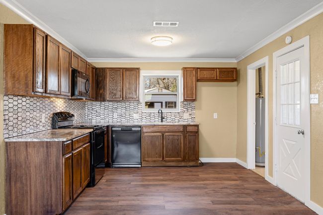Kitchen with visible vents, dark wood finished floors, ornamental molding, black appliances, and backsplash | Image 11