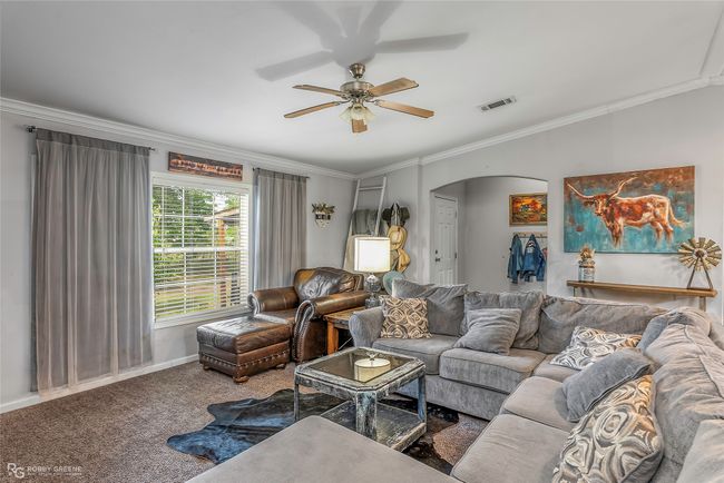 Living area featuring a ceiling fan, visible vents, ornamental molding, arched walkways, and carpet floors | Image 11