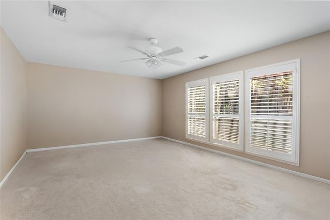 This spacious primary bedroom offers a blank canvas ready for your personal touch. With neutral tones, plush carpeting, and large windows adorned with plantation shutters, the room is filled with natural light and offers a serene retreat. The open layout provides endless possibilities to design your ideal space. | Image 24