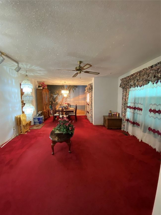 Living room with a textured ceiling, carpet floors, a chandelier, and a ceiling fan | Image 9