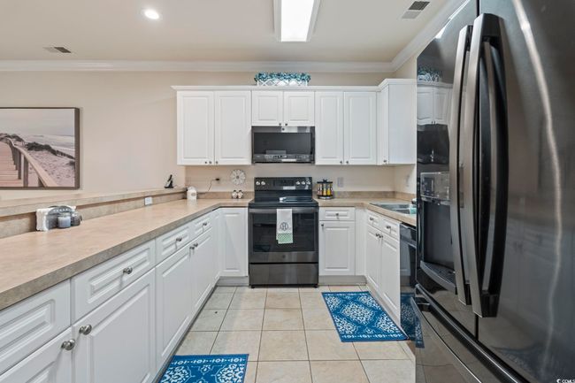 Kitchen with stainless steel appliances, ornamental molding, light countertops, white cabinetry, and light tile patterned flooring | Image 16
