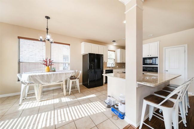 Kitchen featuring black appliances, white cabinetry, light stone countertops, and a chandelier | Image 11