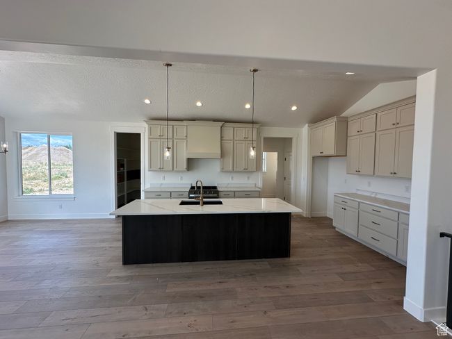 Kitchen featuring light wood finished floors, recessed lighting, an island with sink, decorative light fixtures, and lofted ceiling | Image 7