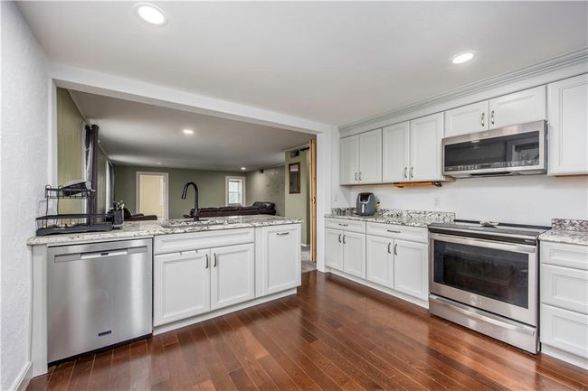 Kitchen featuring light stone countertops, dark wood finished floors, appliances with stainless steel finishes, a peninsula, and a sink | Image 38