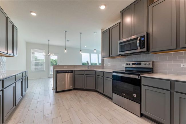 Kitchen featuring stainless steel appliances, decorative backsplash, a peninsula, a chandelier, and light countertops | Image 13