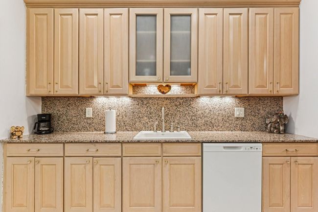 Kitchen with light stone counters, backsplash, a sink, white dishwasher, and light brown cabinets | Image 33